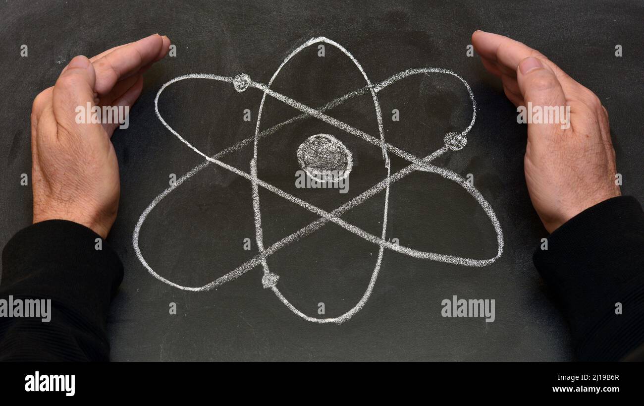Manos rodeando el símbolo del átomo dibujado con tiza en una pizarra Stockfoto