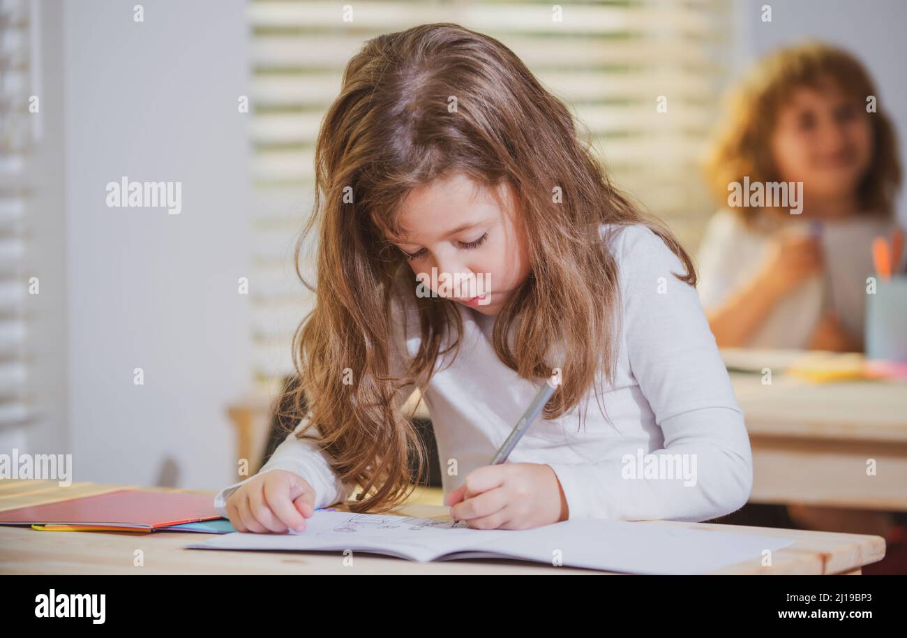Konzentriertes Schulmädchen, das am Schreibtisch sitzt und im Übungsbuch mit Klassenkamerad hinten sitzt. Stockfoto