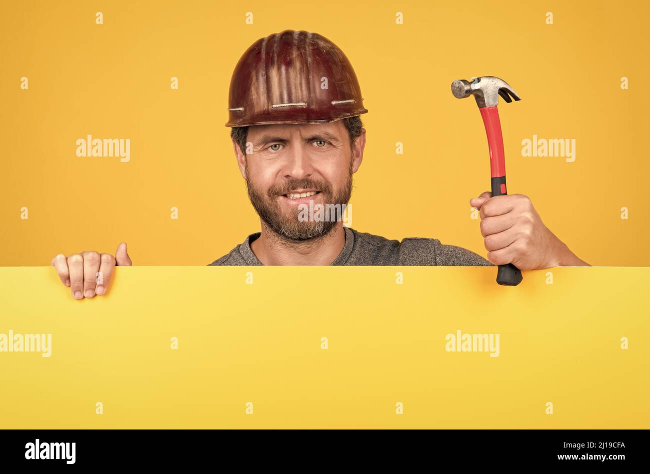 Arbeiterwerbung. Ankündigung. Glücklicher Arbeitstag. Lächelnder Mann im Helm mit Hammer. Stockfoto