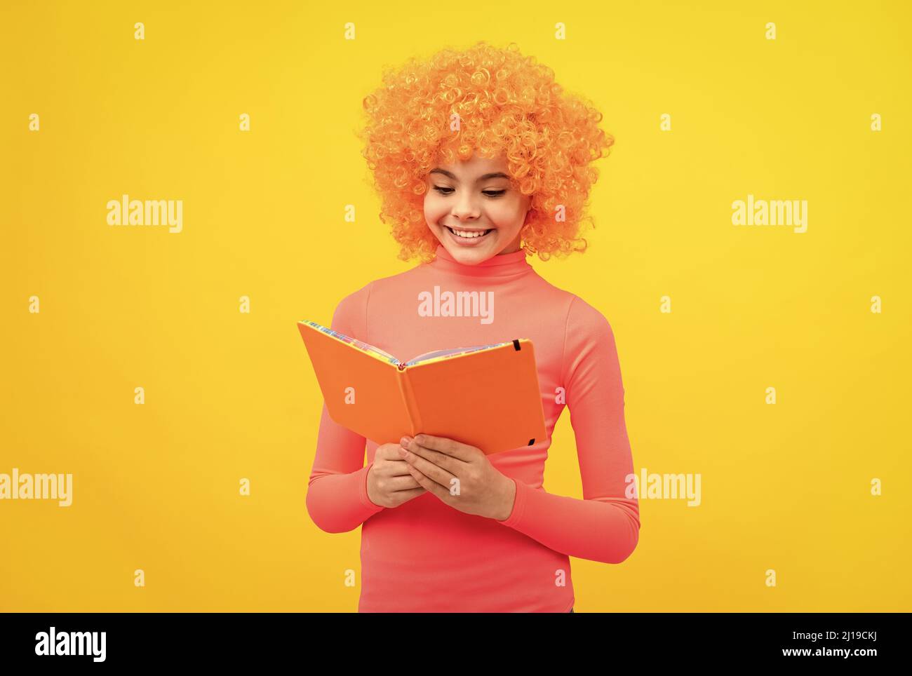 Glückliches Mädchen Kind mit orangen Haaren in rosa Poloneck Lächeln Lesen Schulbuch, Wissen Stockfoto