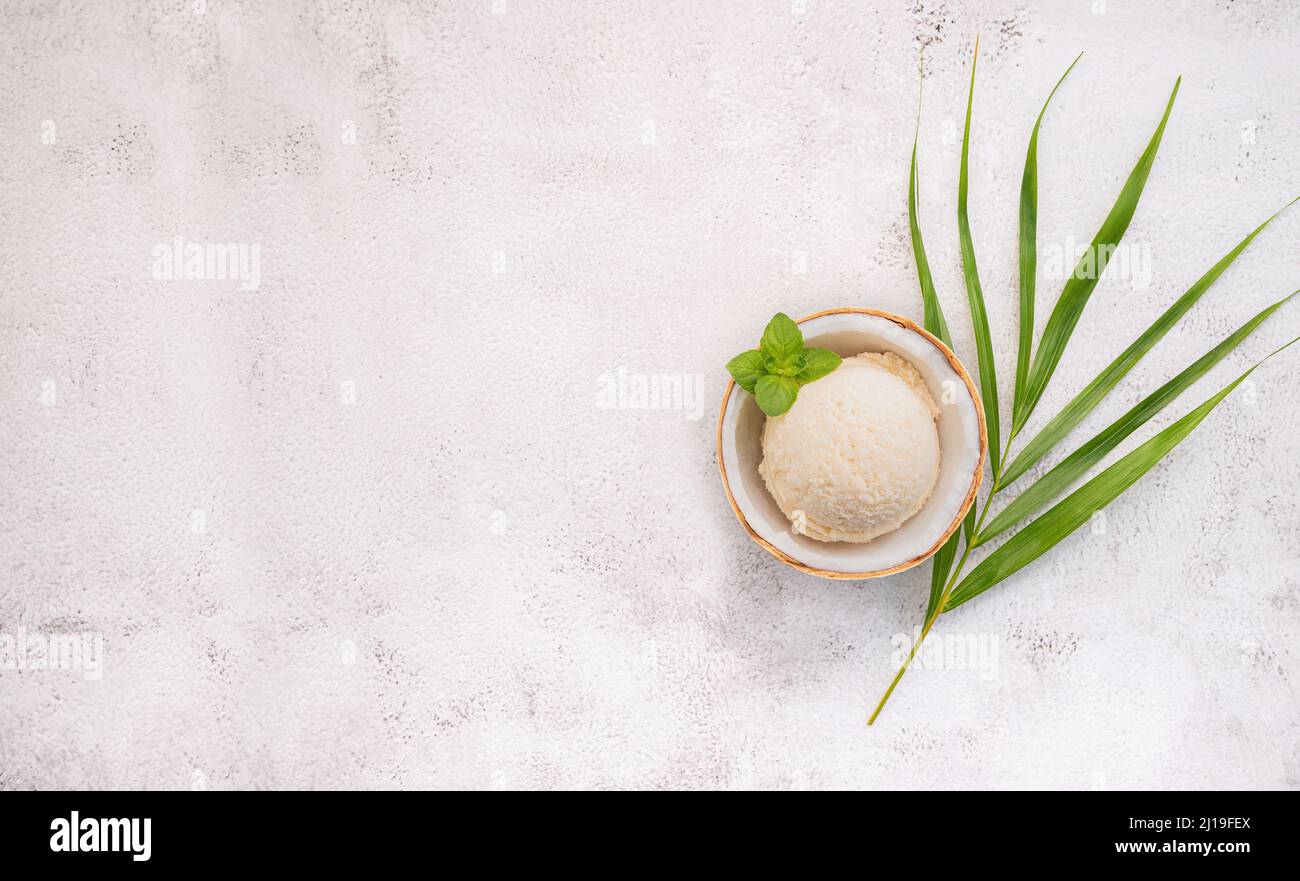 Kokoseis Aromen in der Hälfte der Kokosnuss Setup auf weißem Stein Hintergrund. Sommer und Süße Menükonzept. Stockfoto