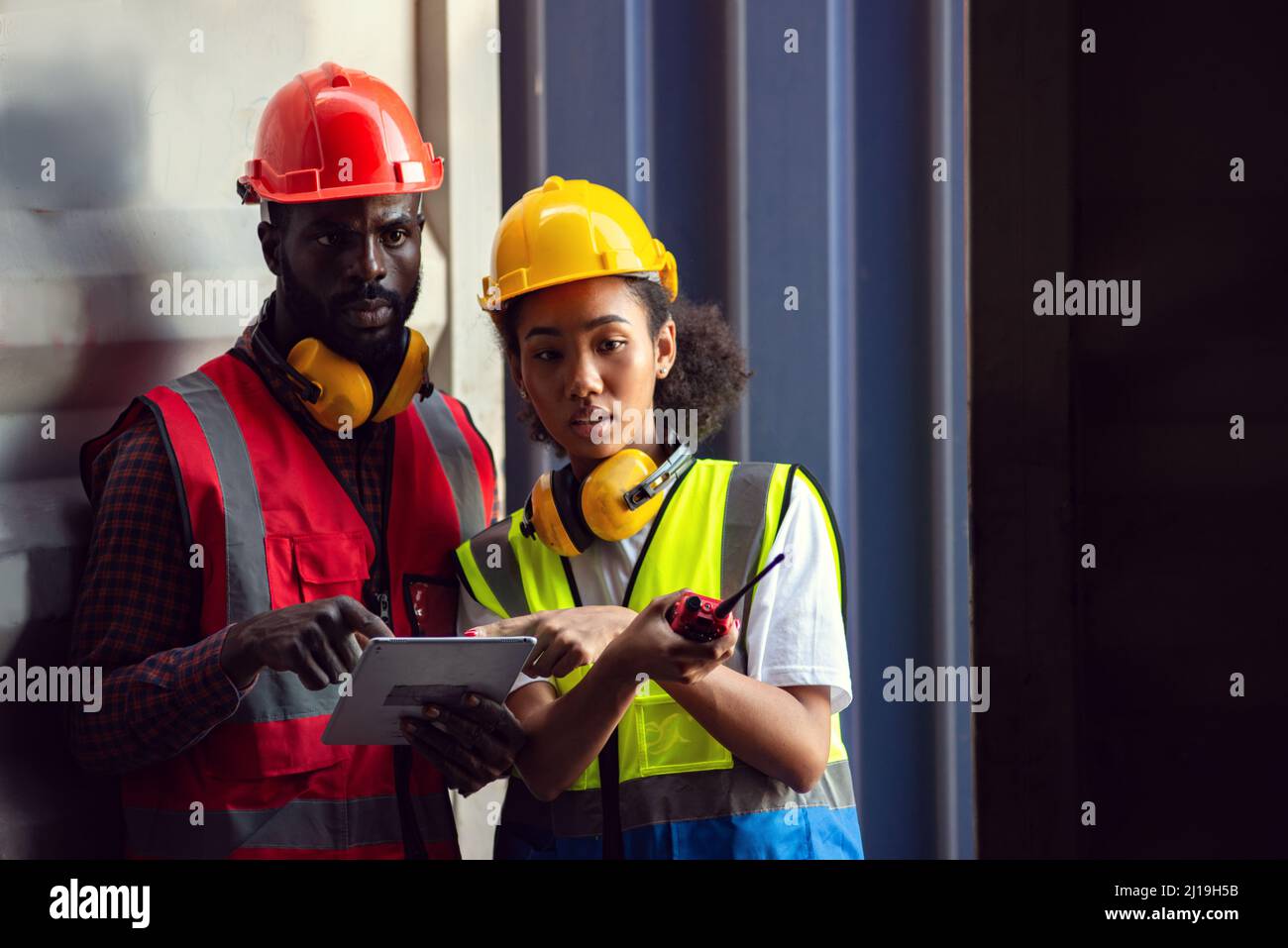 Zwei afroamerikanische Arbeiter, die Tablet-PCs benutzen und kontrollieren, ob Frachtcontainer vom Frachtschiff für den Import geladen werden. Stockfoto