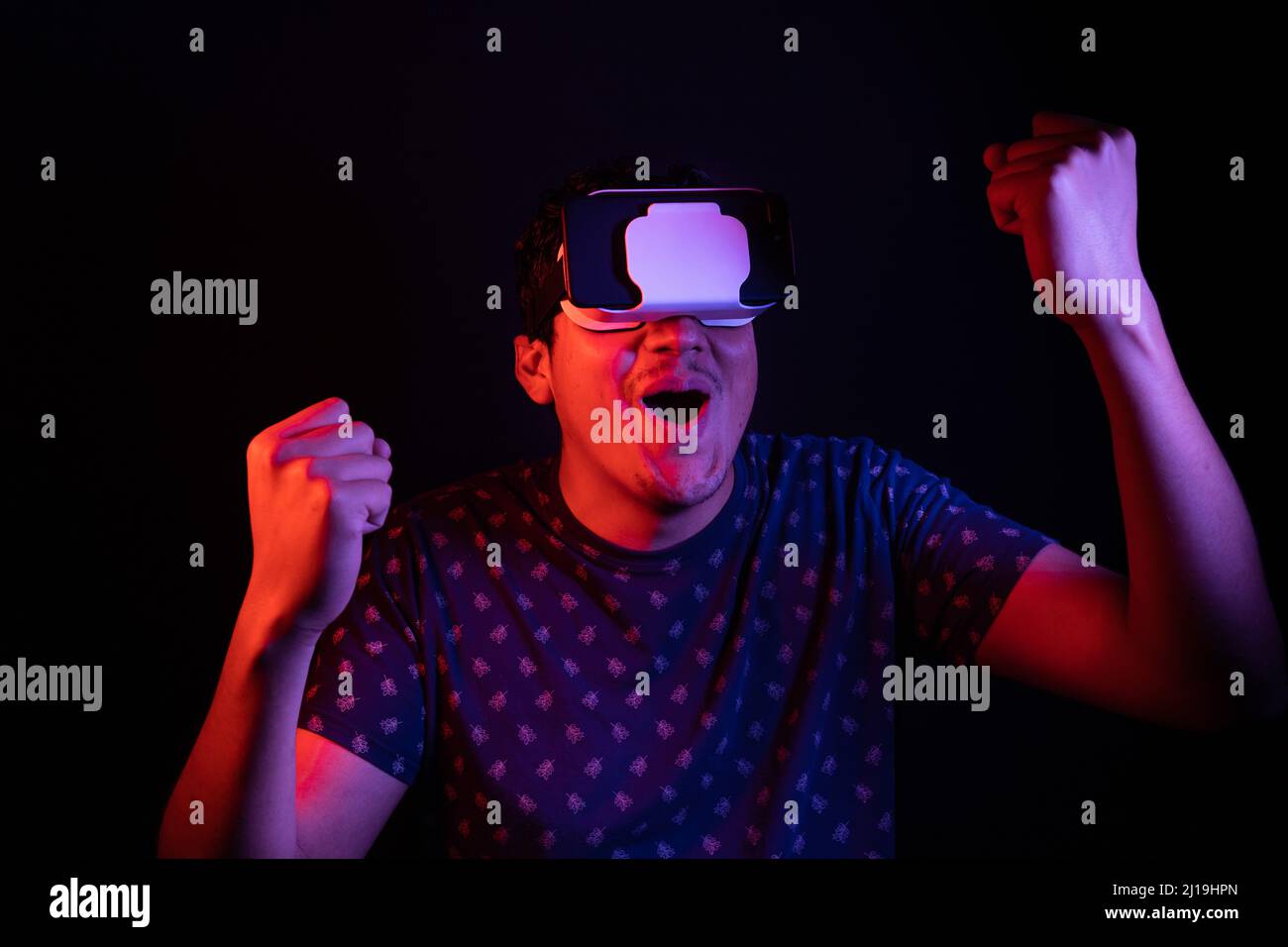 Junger latein verwendet Virtual Reality VR Headset 3D Brille und feiert es mit einem Jubelfest. Dunkle Studiokulisse. Low-Taste Stockfoto