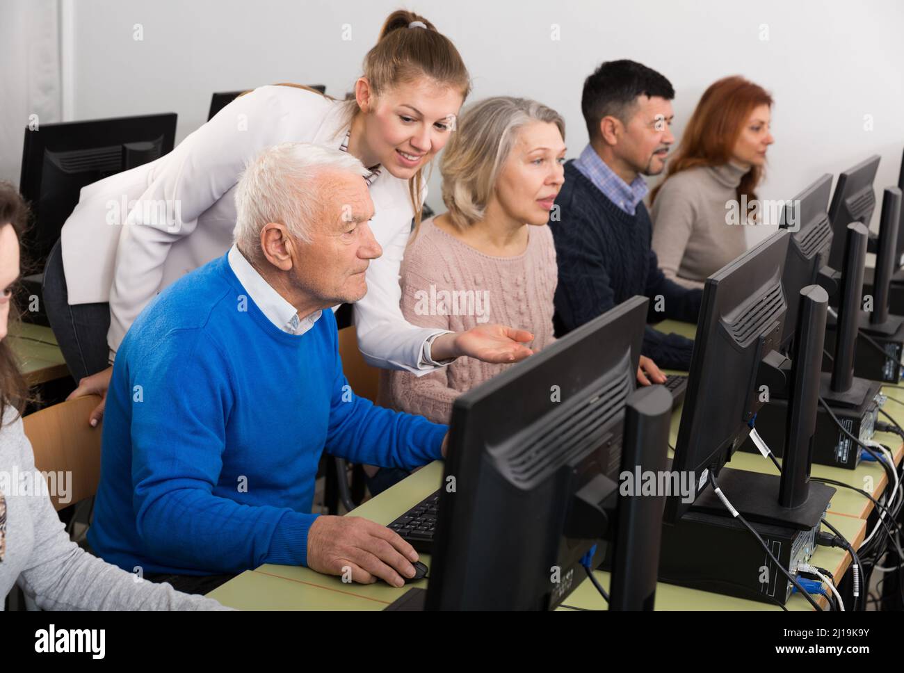 Junge Lehrerin hilft reifen Menschen, Computer zu benutzen Stockfoto