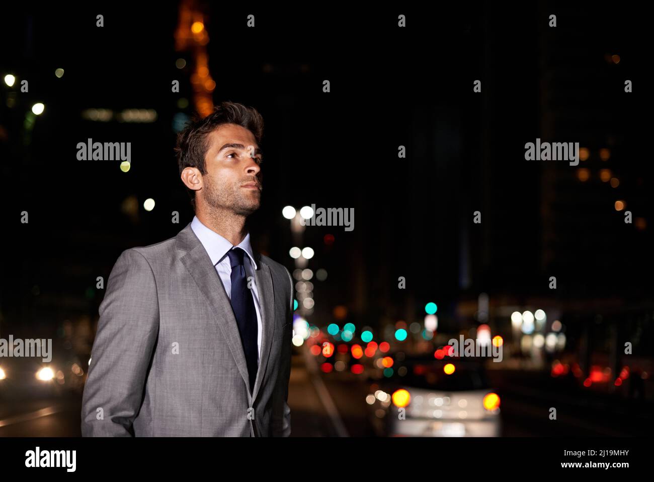 Sie fragen sich, wohin ihn diese Nacht in der Stadt führen wird. Ein gutaussehender Geschäftsmann, der nachts mitten in einer belebten Straße steht. Stockfoto