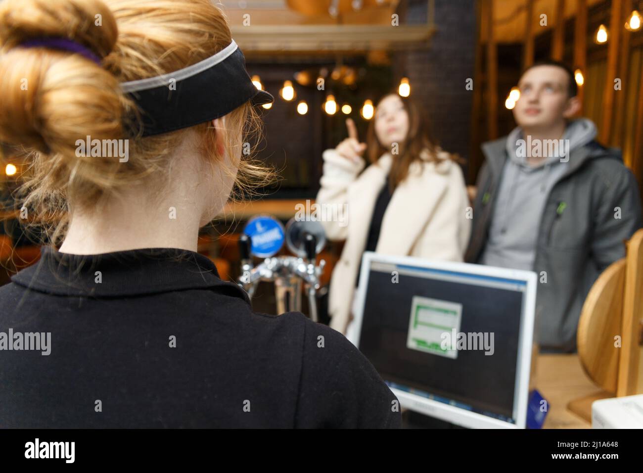 Ein Café-Mitarbeiter nimmt eine Bestellung von nicht erkennbaren Besuchern mit einem automatisierten Computersystem an. Stockfoto