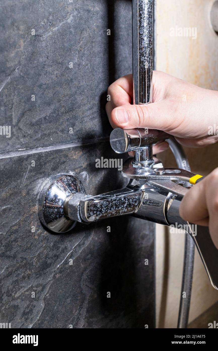 Klempner repariert alten Duschhahn an gefliesten Wänden zu Hause Stockfoto