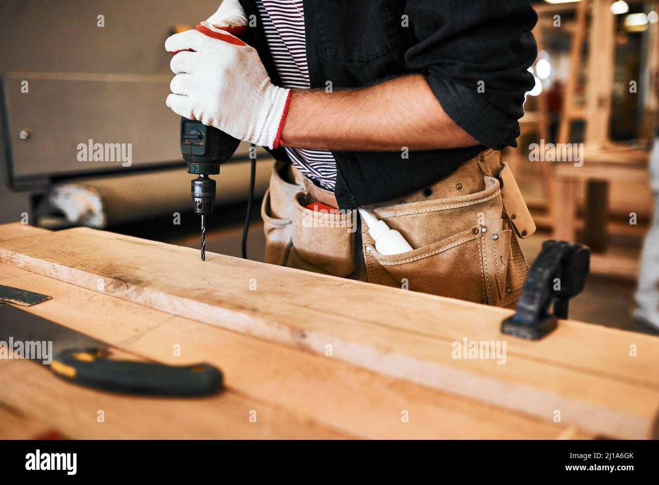 Alles ist vom Bohrer getrennt. Ausgeschnittene Aufnahme eines unerkennbaren Zimmermanns mit einer elektrischen Bohrmaschine in einer Werkstatt. Stockfoto