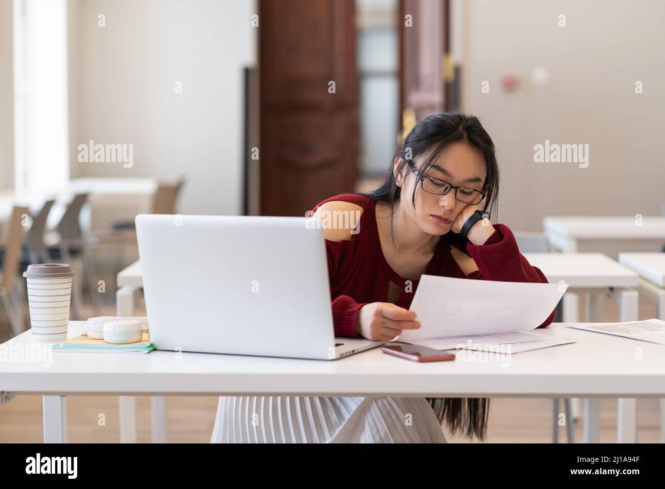 Müde gelangweilt asiatische weibliche Student lesen gedruckte Papiermaterialien während des Studiums in der Bibliothek Stockfoto