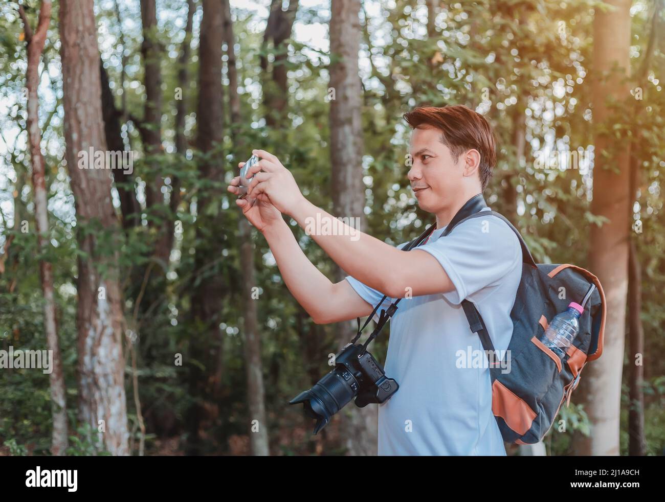 Ein männlicher Tourist, der eine Handtasche, eine Wasserflasche und eine Kamera trägt, geht durch den Wald. Stockfoto