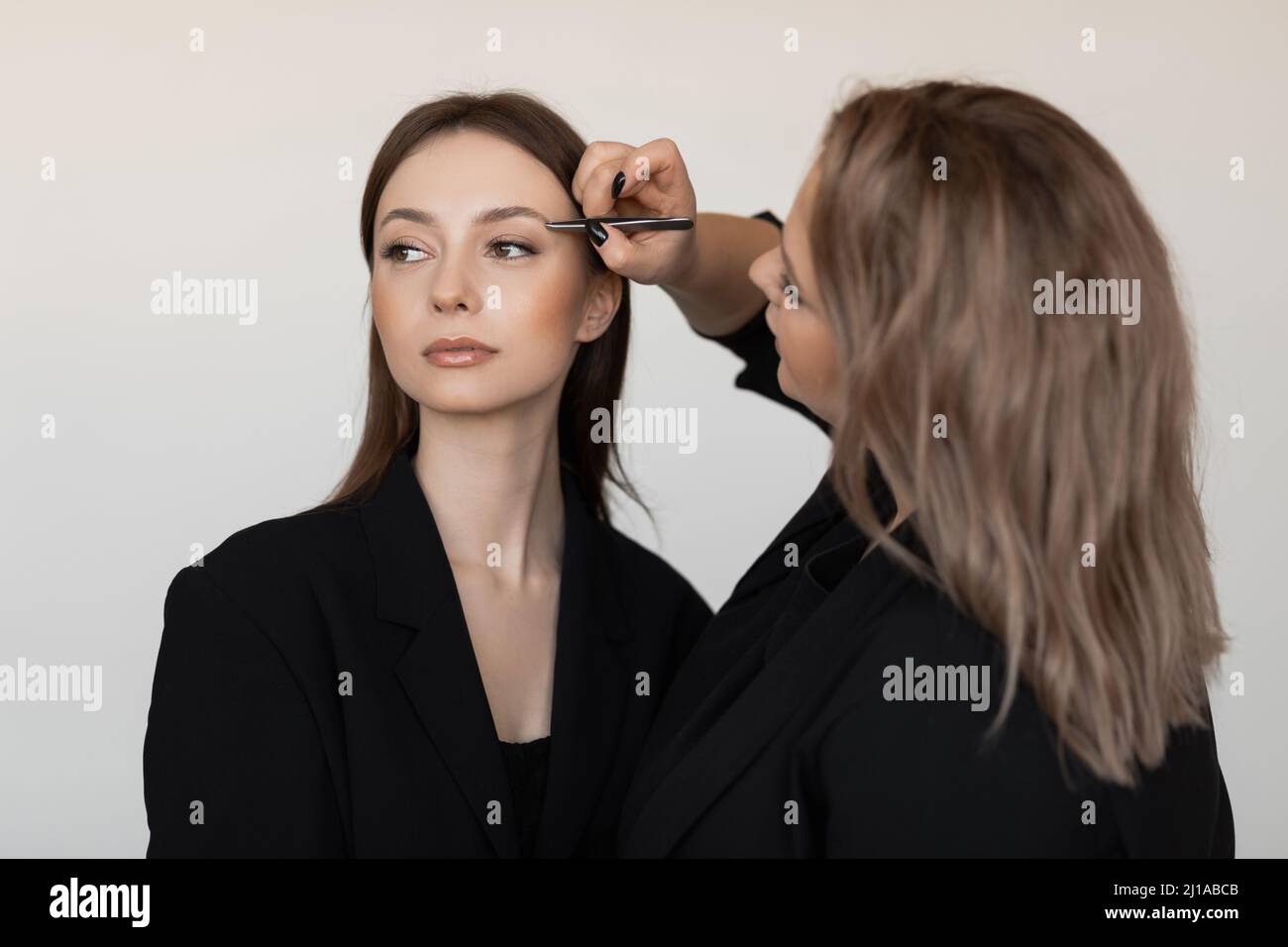 Professionelle attraktive Make-up-Künstler pinkiert Augenbrauen von jungen gut aussehende Frau Modell. Make-up, Werbung. Stockfoto