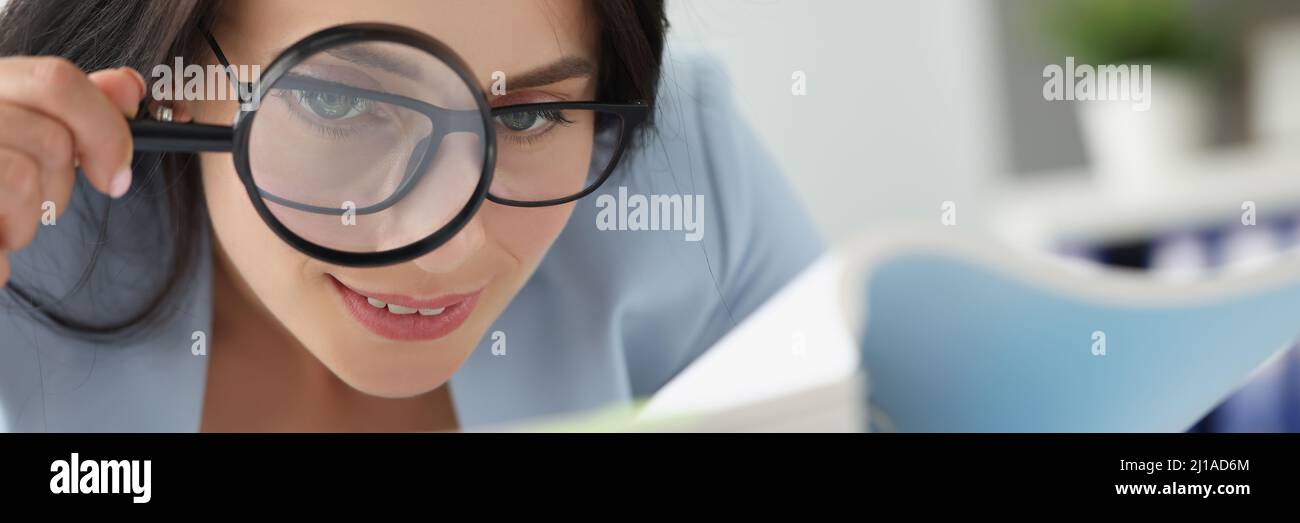 Frau, die Dokumente in einem Ordner durch eine Lupe betrachtet Stockfoto