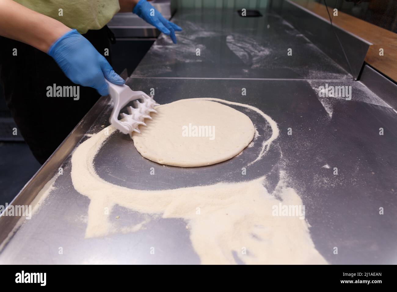 Der Koch verarbeitet den Pizzateig mit einer speziellen Walze mit Spikes, um den Teig flauschig und knusprig zu machen. Stockfoto