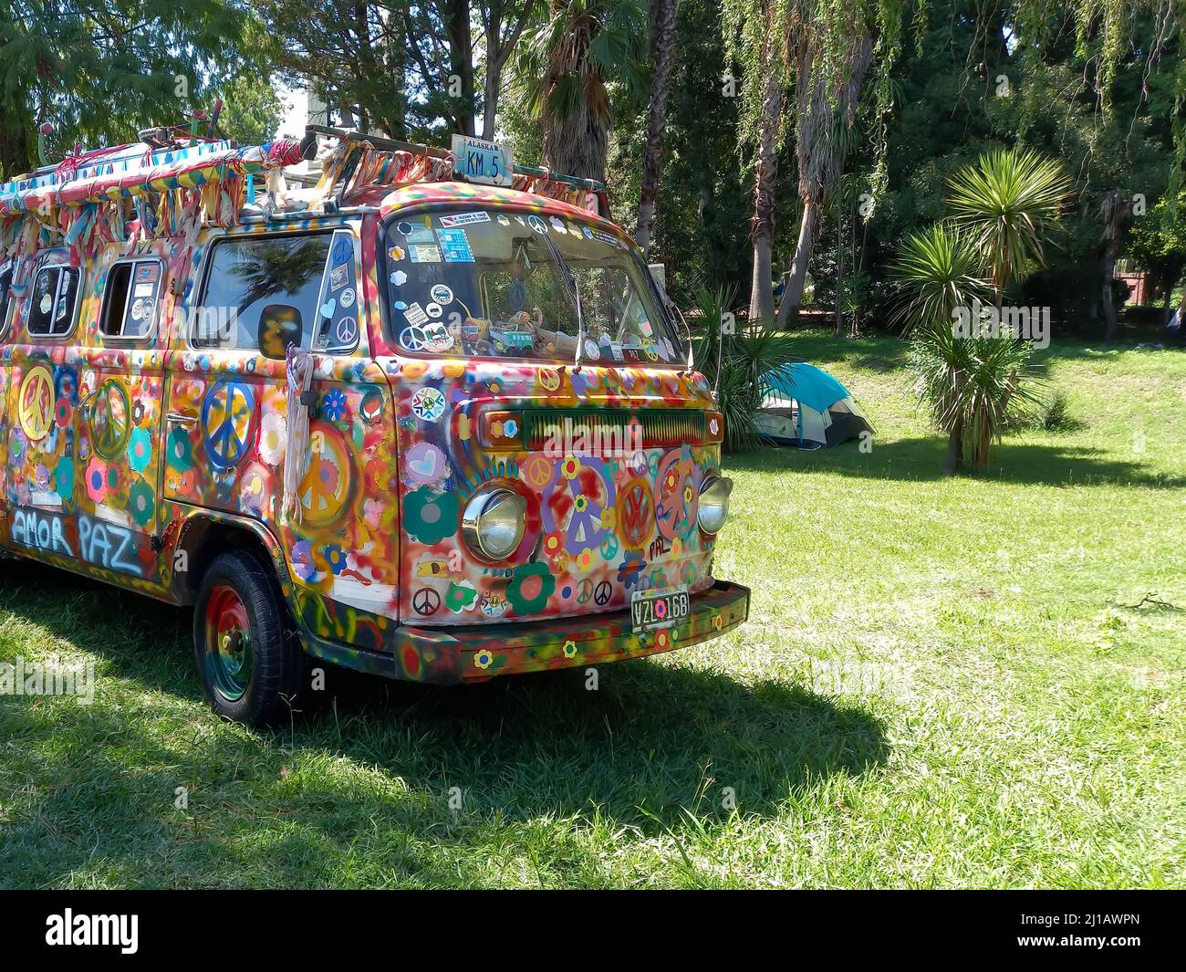 Alte bunte Blume Power Hippie van Volkswagen Kombi Camper 1960s auf einem Campingplatz. Liebe und Frieden Symbole. Bäume Gras Natur Hintergrund. Copyspace Stockfoto