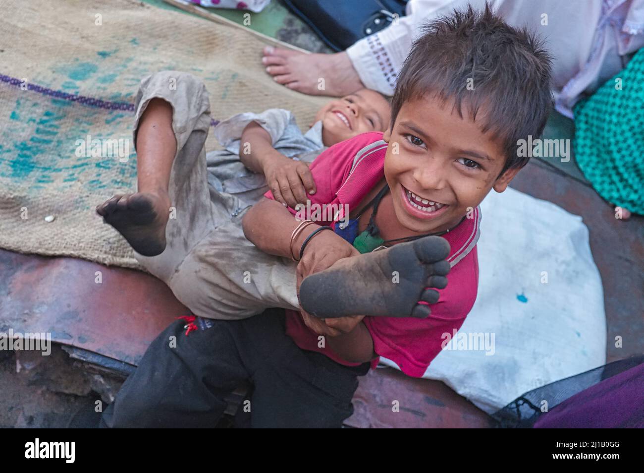 Verspielte Kinder im Slum-Gebiet von Darukhana in Mumbai, Indien, wobei einer fröhlich seine schmutzigen Füße abweist Stockfoto