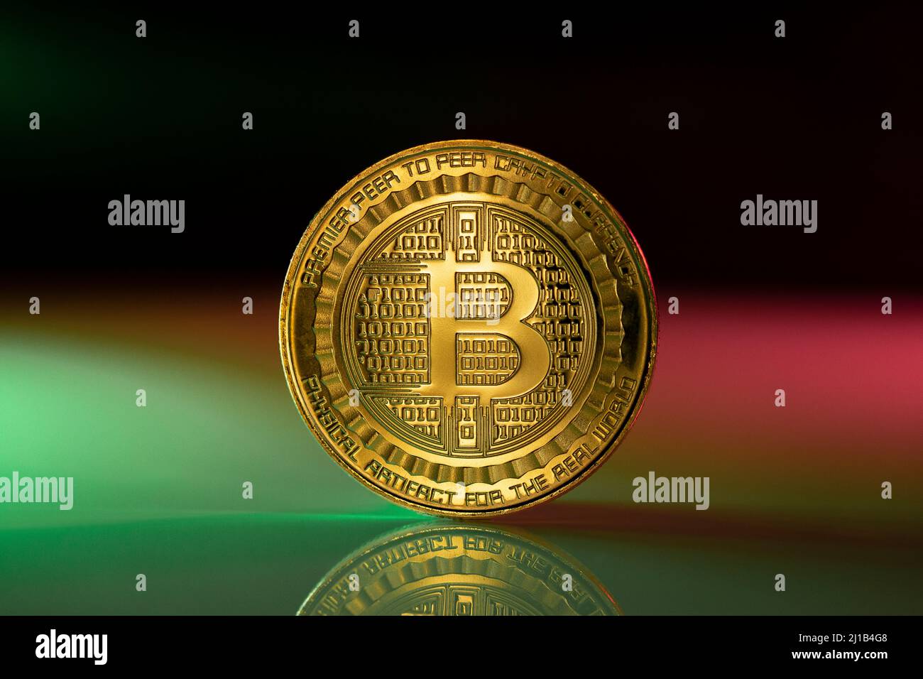 Bitcoin BTC Kryptowährung physische Münze auf der reflektierenden Oberfläche platziert und mit grünen und rosa Lichtern beleuchtet. Stockfoto