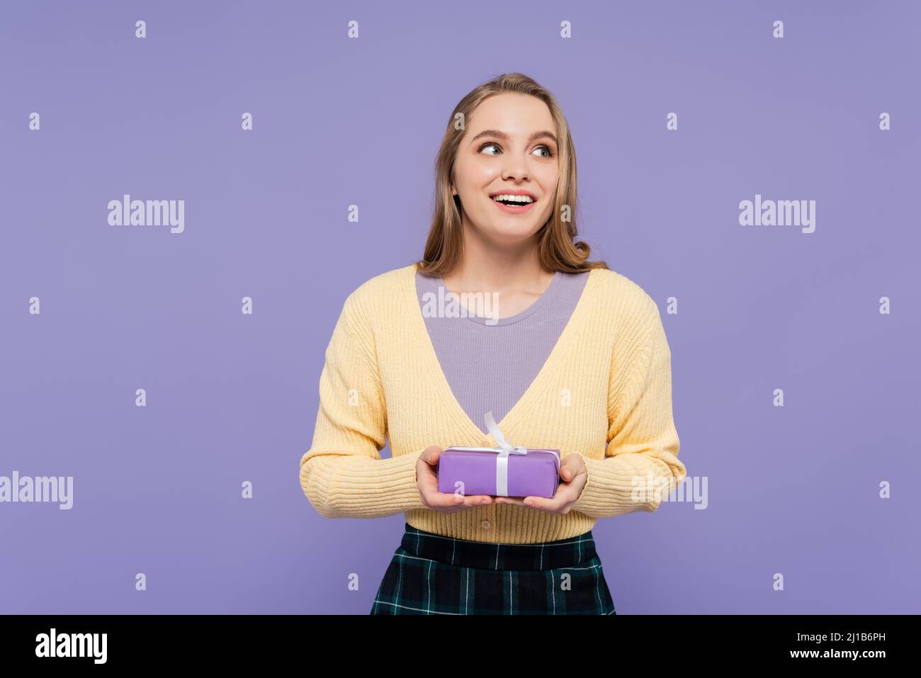 Aufgeregt junge Frau hält verpackte Geschenkbox isoliert auf lila Stockfoto