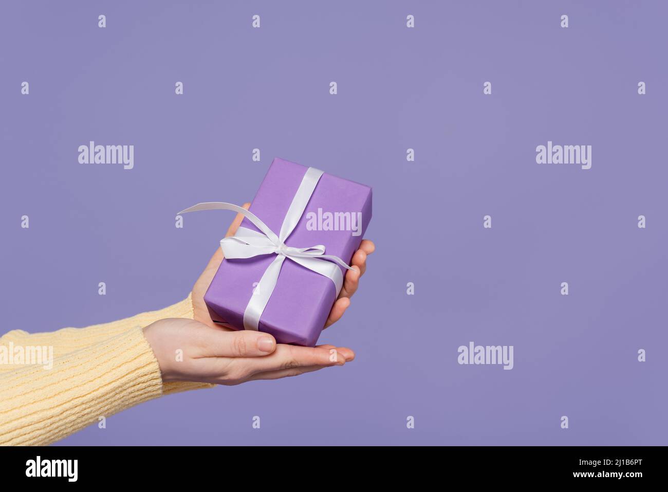 Beschnittene Ansicht der jungen Frau hält eingewickelte Geschenkbox in Händen isoliert auf lila Stockfoto