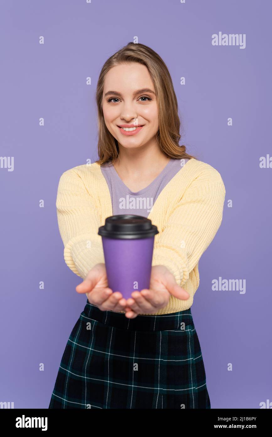 Glückliche junge Frau hält Kaffee in Papierbecher isoliert auf lila gehen Stockfoto