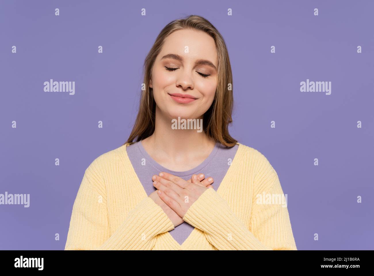 Zufrieden junge Frau mit geschlossenen Augen berühren Brust isoliert auf lila Stockfoto