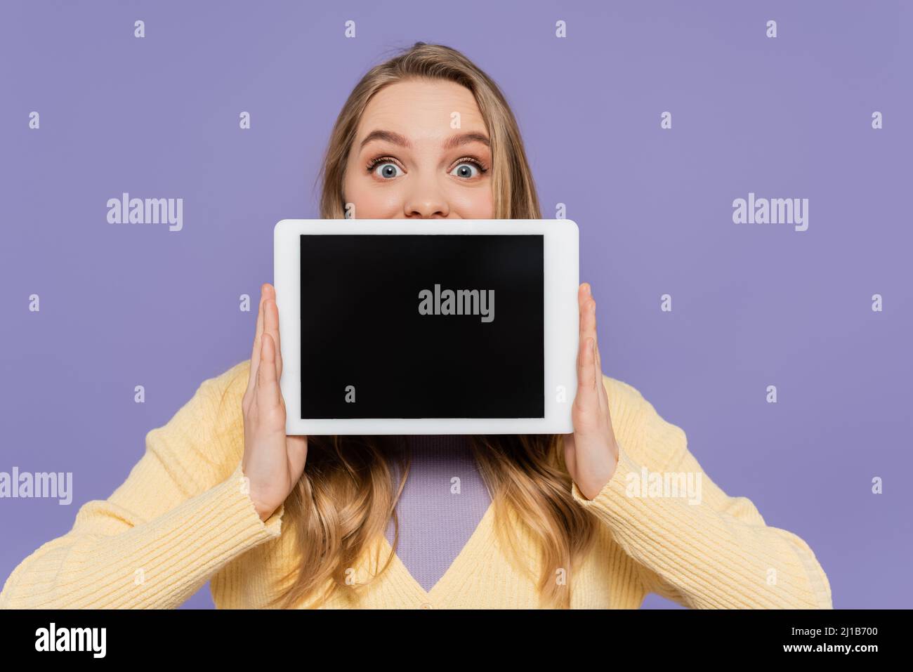 Junge Frau bedeckt den Mund und hält ein digitales Tablet mit einem leeren Bildschirm, der auf violett isoliert ist Stockfoto
