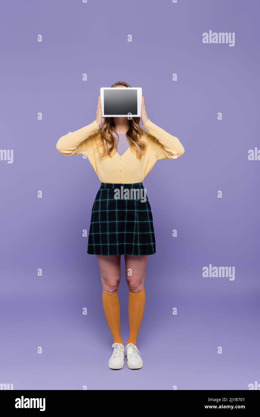 Junge Frau bedeckt das Gesicht, während sie das digitale Tablet mit leerem Bildschirm auf lila hält Stockfoto