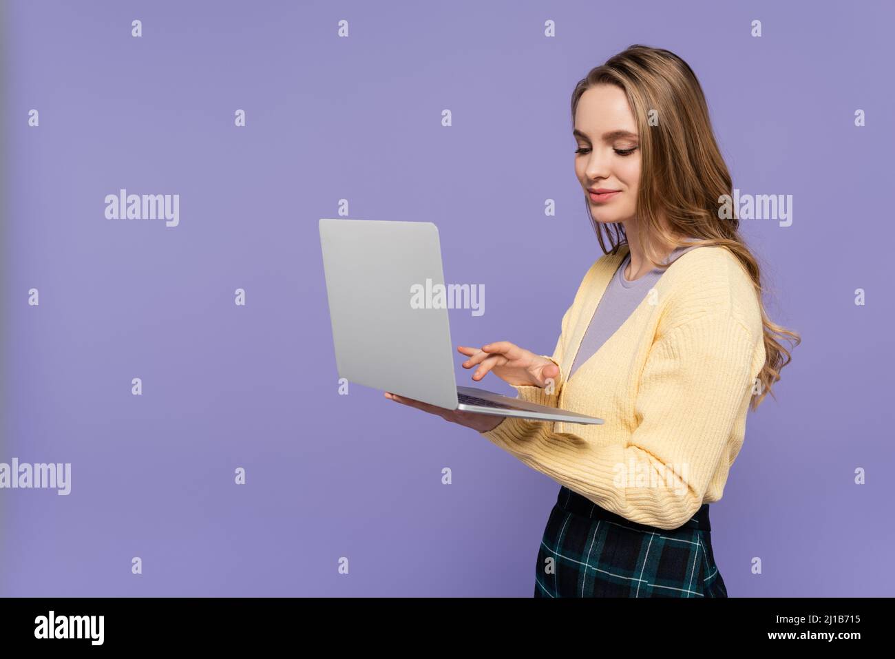 Fröhlicher Student mit Laptop isoliert auf lila Stockfoto