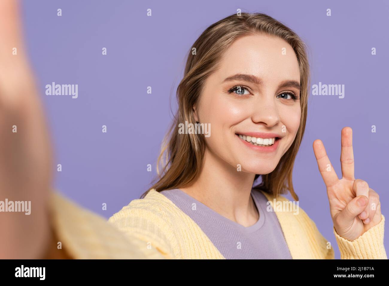 Fröhliche junge Frau, die auf violettem Purpur ein Friedenszeichen zeigt Stockfoto