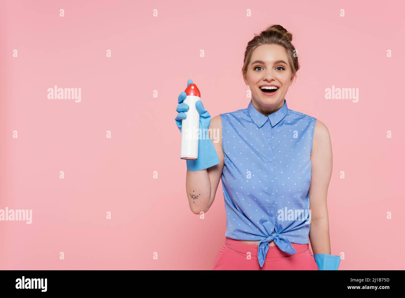 Aufgeregt junge Frau in Gummihandschuhen halten Lufterfrischer Flasche isoliert auf rosa Stockfoto