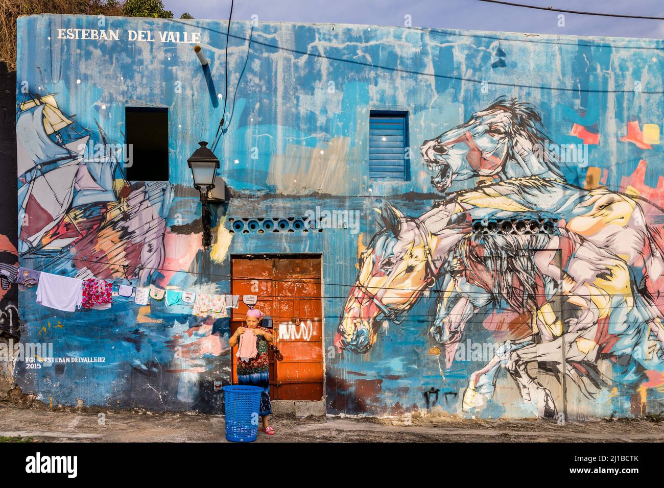 FRAU, DIE IHRE WÄSCHE ZUM TROCKNEN AUFHÄNGTE, BEMALTE WÄNDE IM VIERTEL ATARAZANA, EINEM KOLONIALVIERTEL, DAS VON DER UNESCO, SANTO DOMINGO, DOMINIKANISCHE REPUBLIK, ZUM WELTKULTURERBE ERKLÄRT WURDE Stockfoto