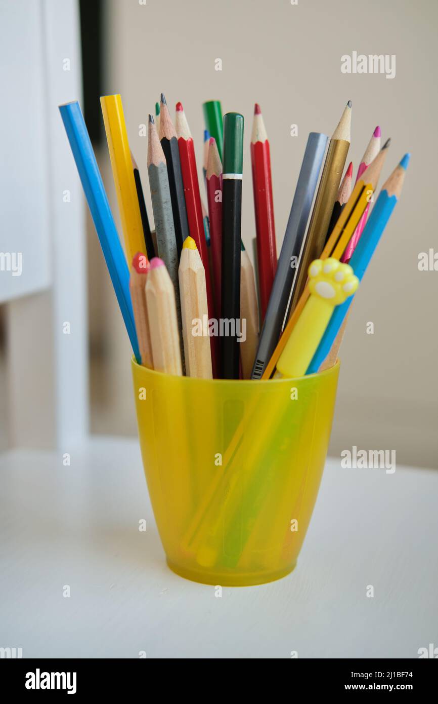 Gelbes Glas mit Buntstiften und lustigen Stiften Stockfoto