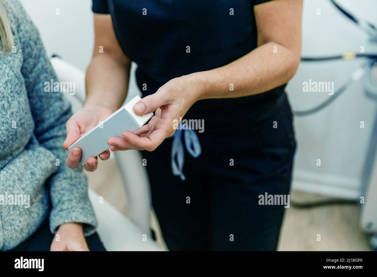 Eine Krankenschwester in einem medizinischen Wellness-Spa, die dem Patienten oder Kunden ein Anti-Aging-Hautpflegeprodukt zeigt Stockfoto