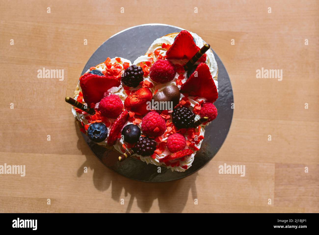Herzförmiger Kuchen mit roten reifen Erdbeeren und frischen Himbeeren und Blaubeeren. Valentinstag, Muttertag oder Geburtstagskuchen mit Stockfoto