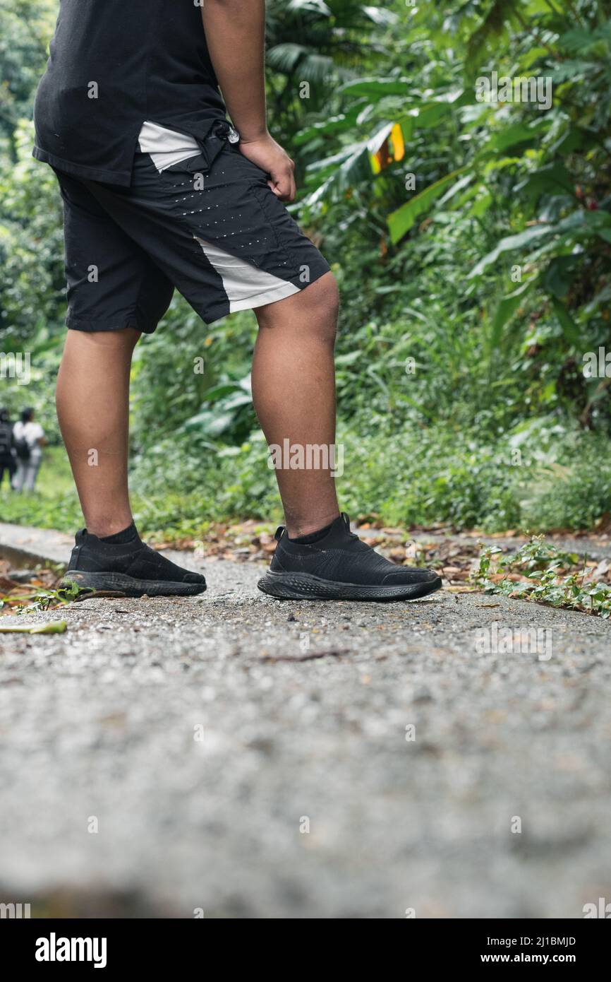 Aufnahme der Füße eines jungen Mannes, der sich in der Mitte der Straße nach einem langen Weg ausruht. Junge, der andere Menschen in der Mitte des Kolumbianers beobachtet Stockfoto