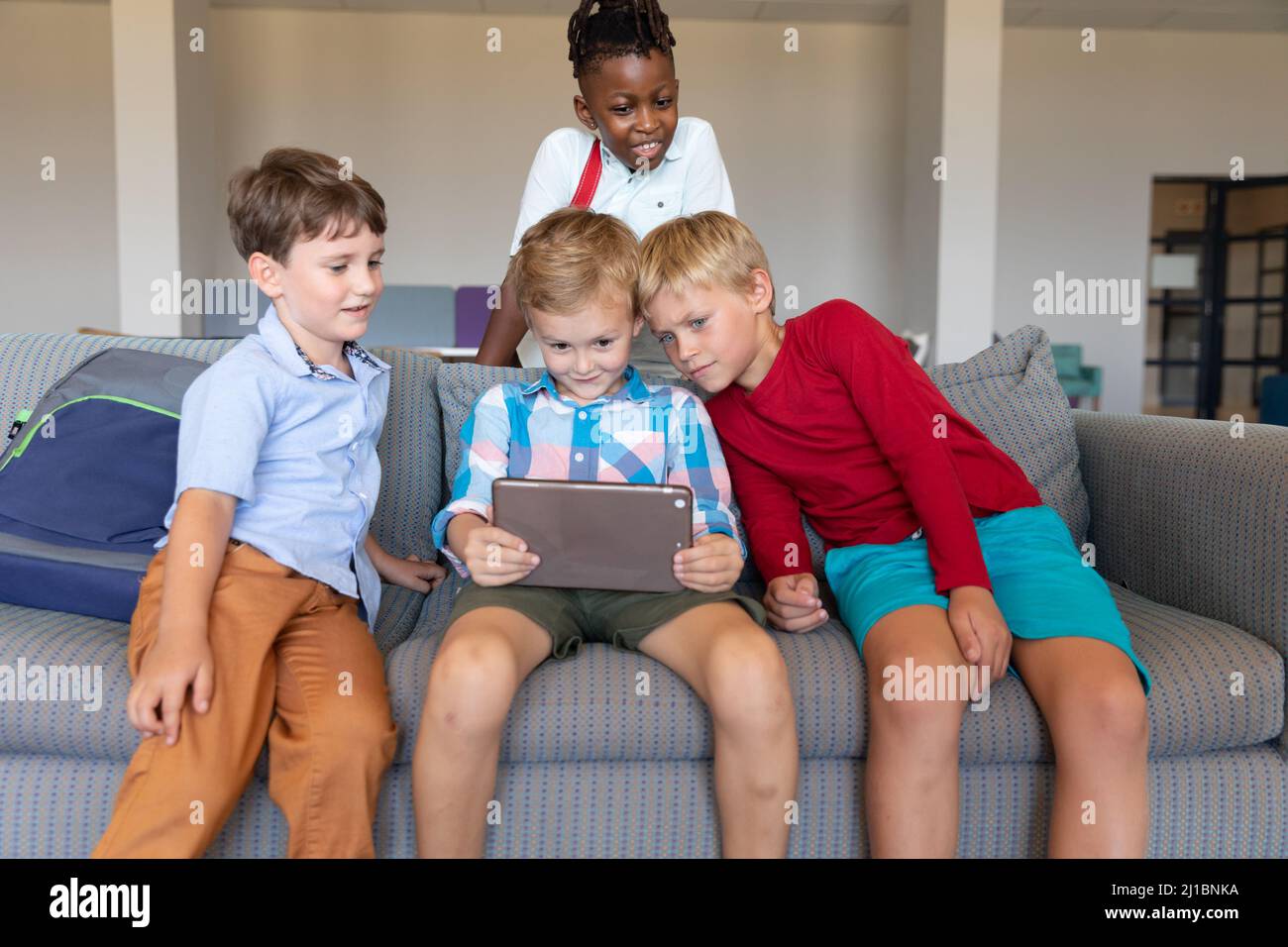 Multirassische Grundschüler, die in der Schule auf dem Sofa sitzen und ein digitales Tablet betrachten Stockfoto