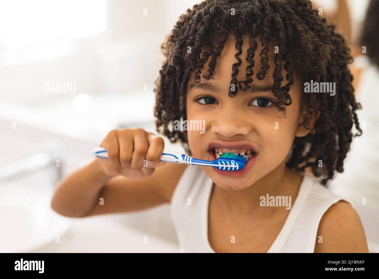 Porträt eines hispanischen, lockigen Jungen, der zu Hause im Badezimmer Zähne putzt Stockfoto