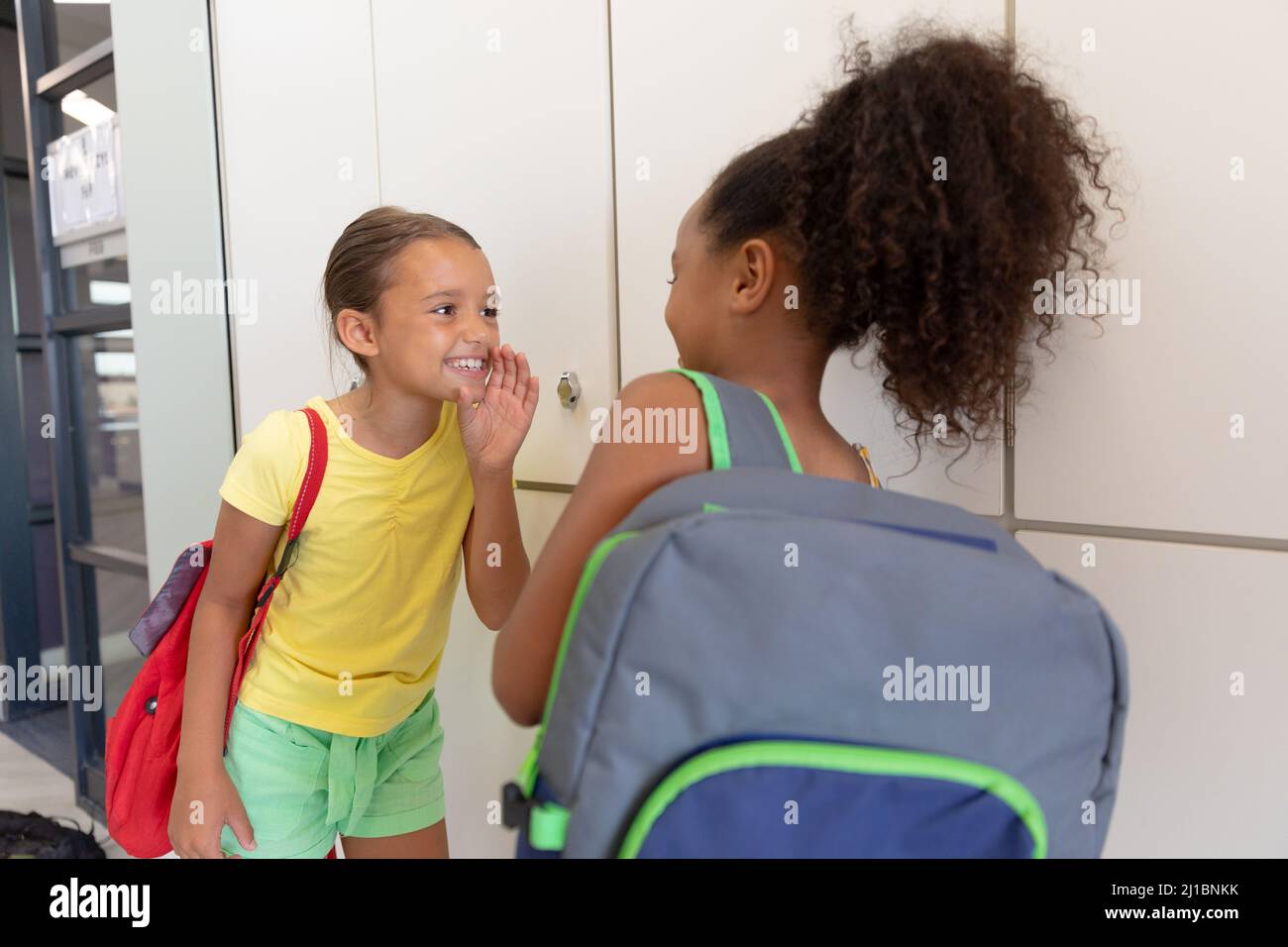 Multirassische Grundschüler, die im Schulflur neben Schließfächern stehen, plaudern Stockfoto