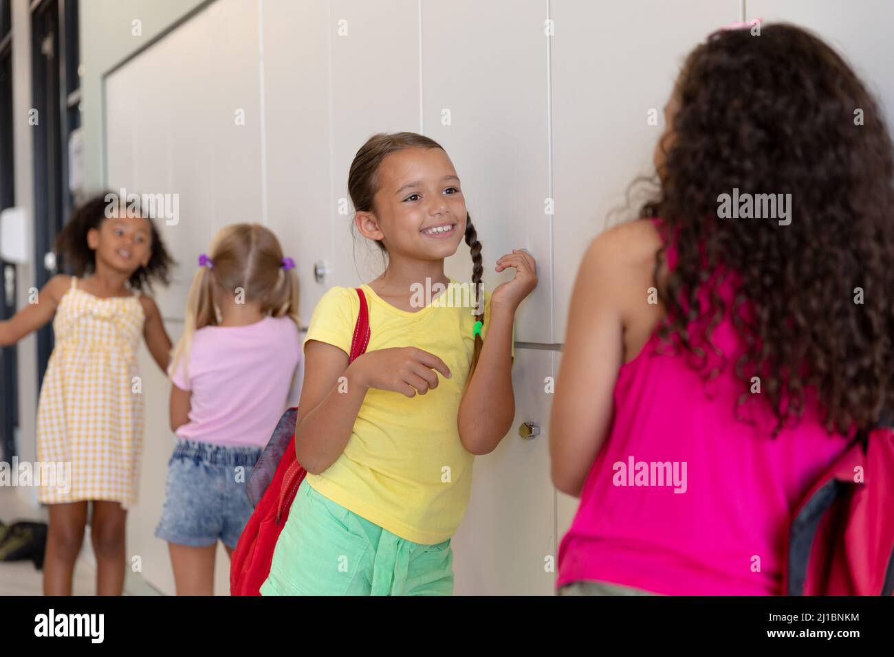 Multirassische Grundschüler sprechen, während sie an Schließfächern im Schulkorridor stehen Stockfoto
