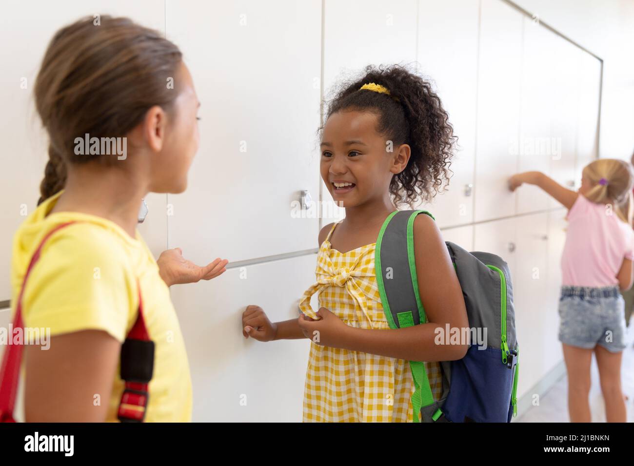 Glückliche multirassische Grundschüler sprechen, während sie an Schließfächern im Schulkorridor stehen Stockfoto