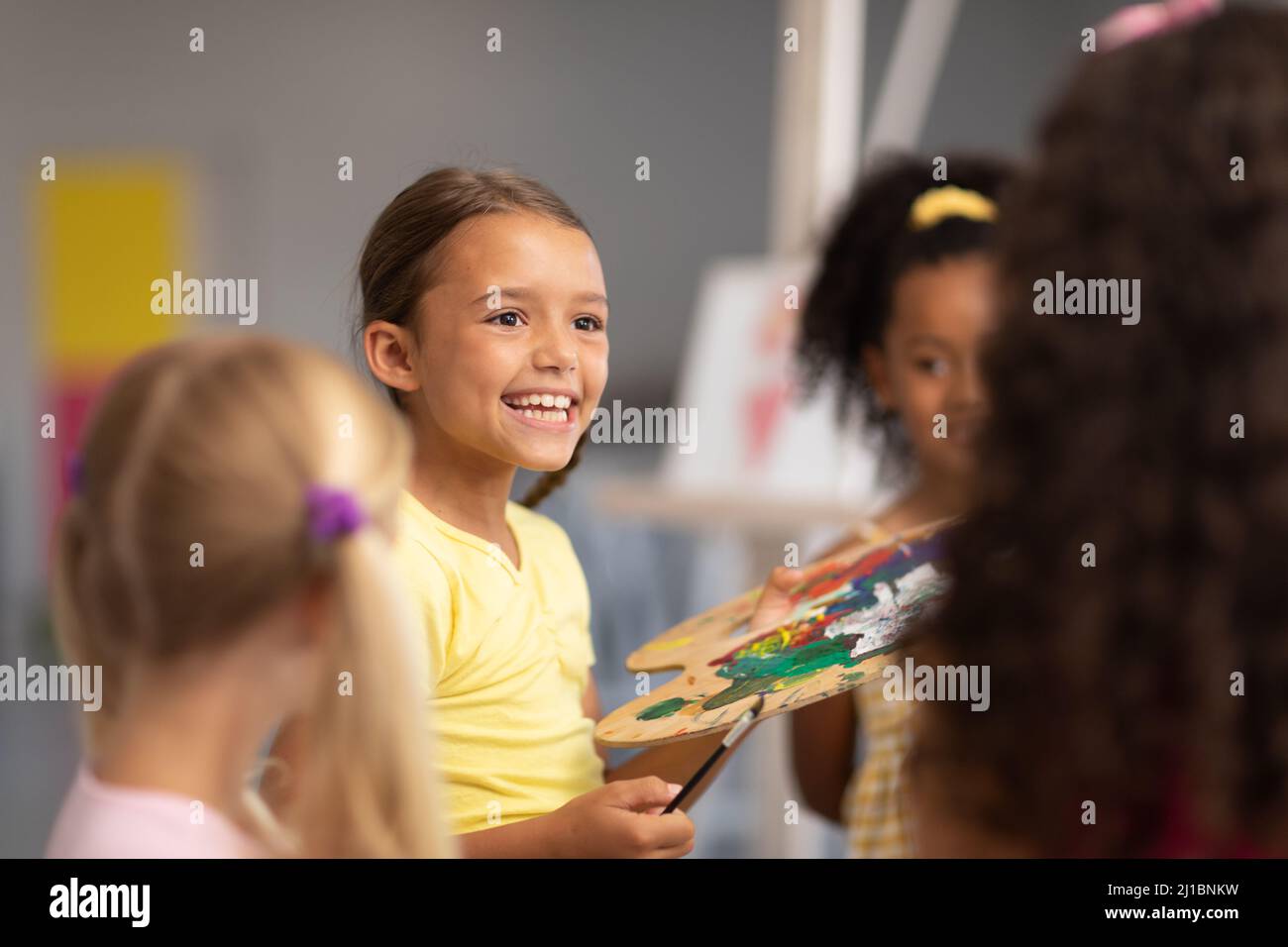 Fröhliches kaukasisches Grundschülerin, das während der Zeichnungsklasse von multirassischen Klassenkameraden sitzt Stockfoto
