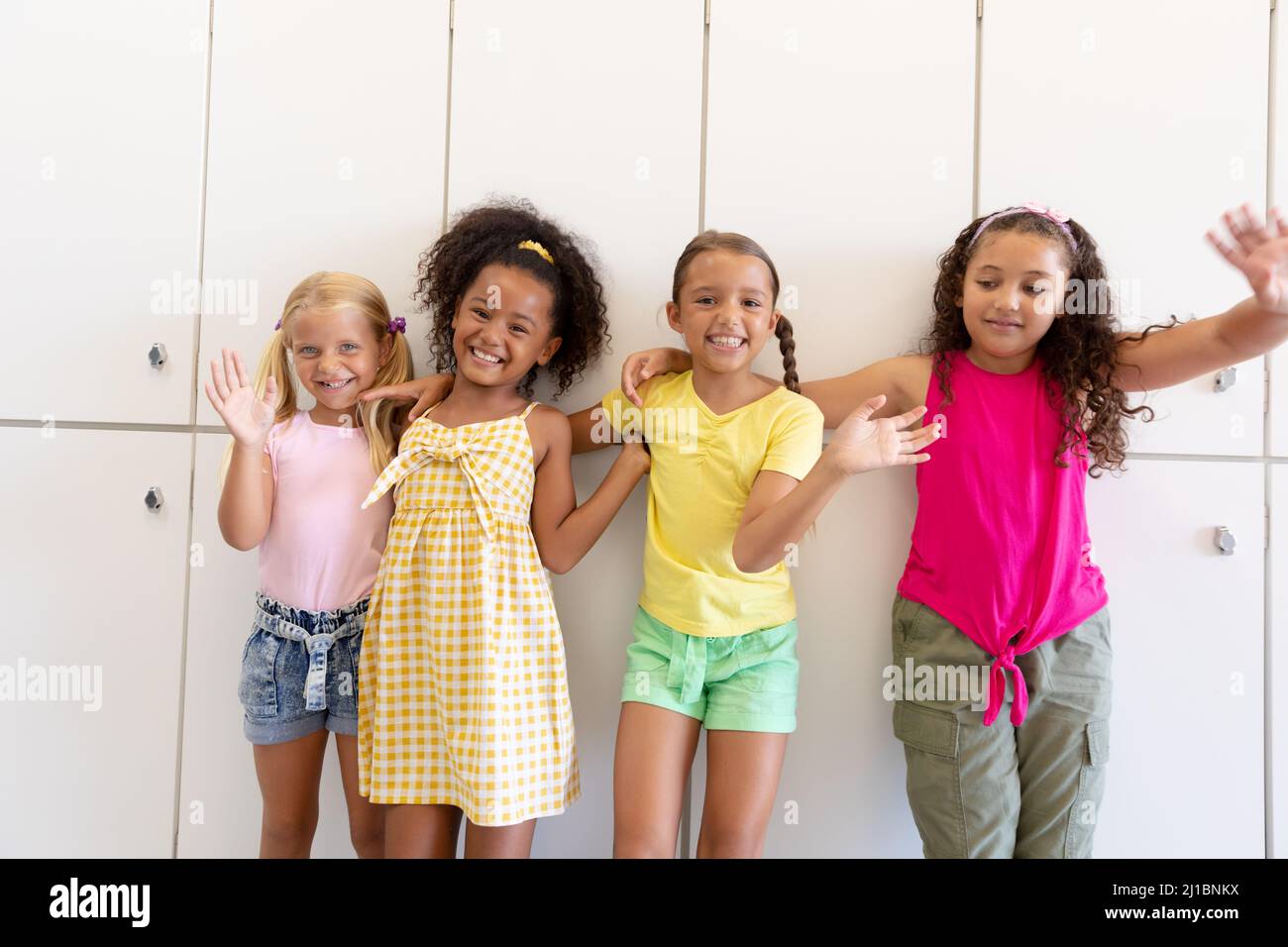 Portrait von fröhlichen niedlichen multirassischen Grundschülerin mit Arm um warten, während stehen Stockfoto