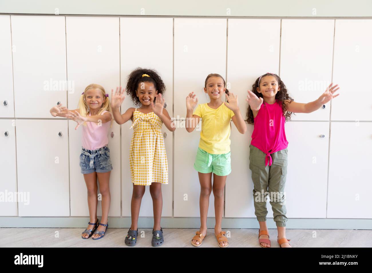 Porträt von fröhlichen multirassischen Grundschülerin, die gestikuliert, während sie gegen Schließfächer steht Stockfoto