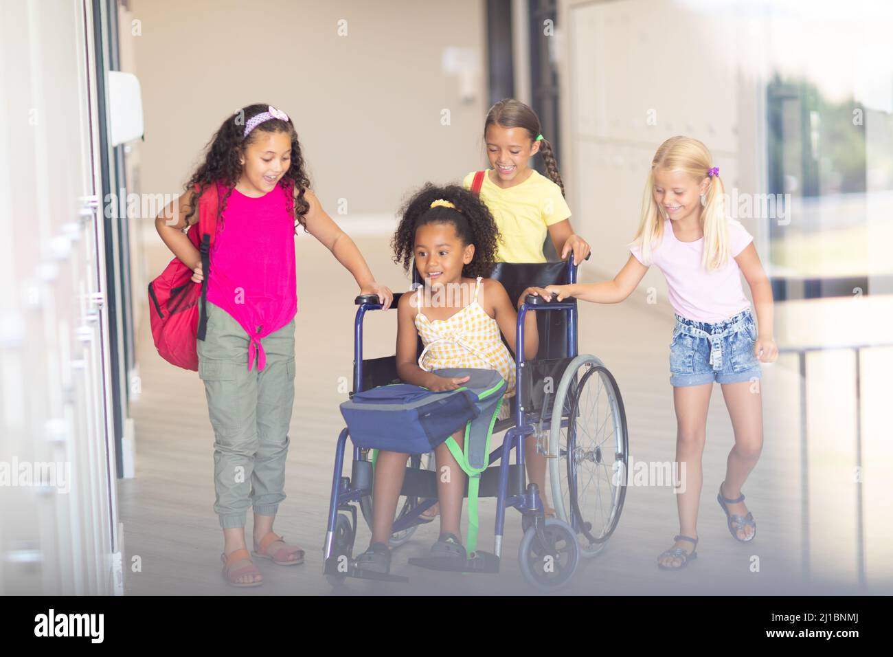 Lächelnde multirassische Grundschüler, die weiblichen Biracial-Klassenkameraden im Rollstuhl helfen Stockfoto