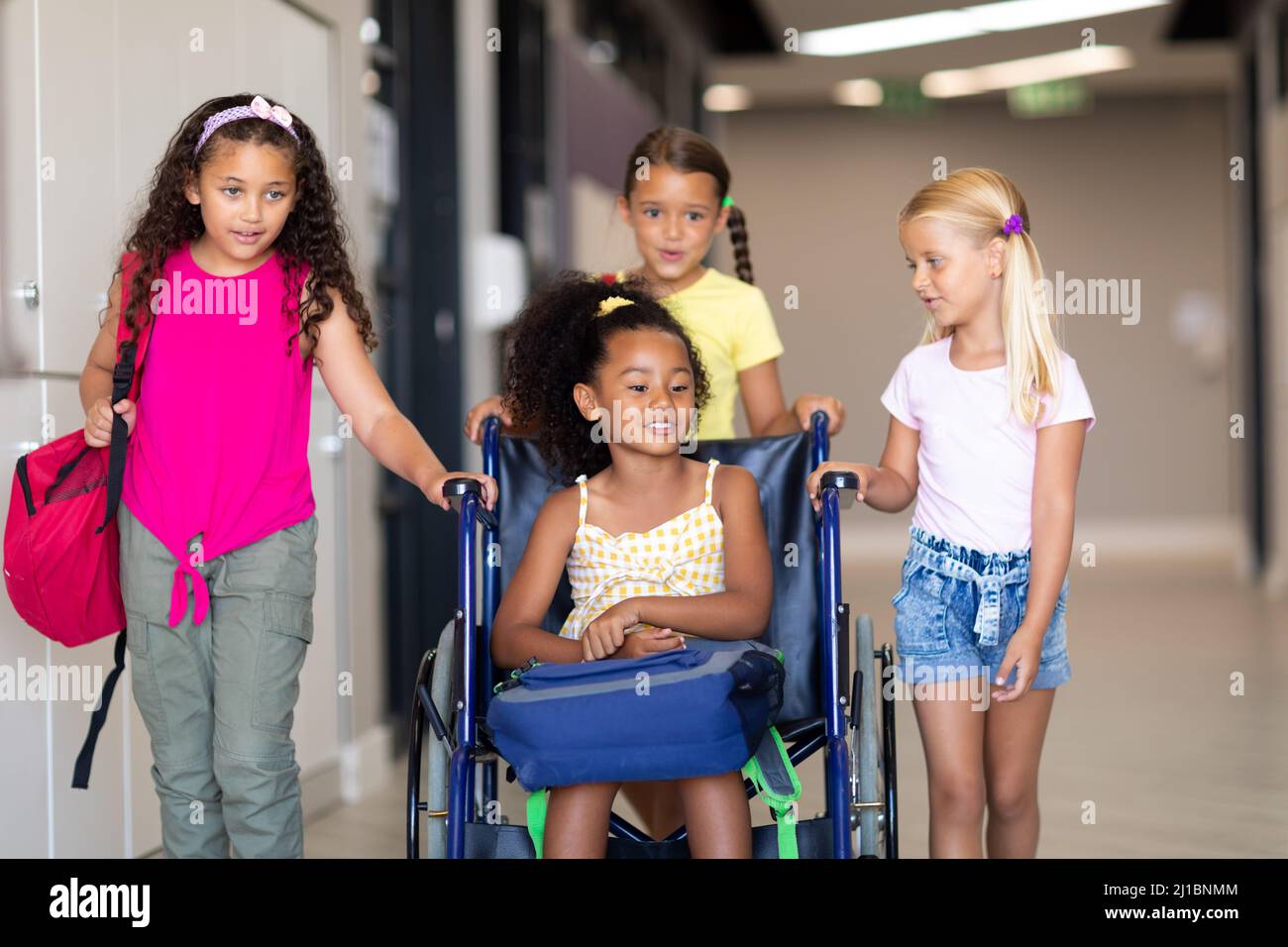 Multirassische Grundschüler, die weiblichen Biracial Klassenkameraden auf dem Rollstuhl sitzend helfen Stockfoto