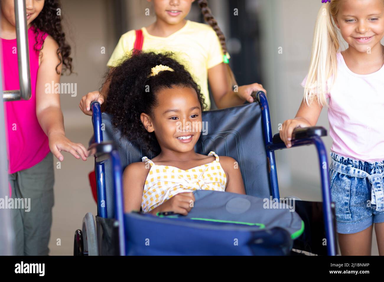Biracial Grundschule Schülerinnen sitzen auf Rollstuhl mit multirassischen Klassenkameraden halten es Stockfoto