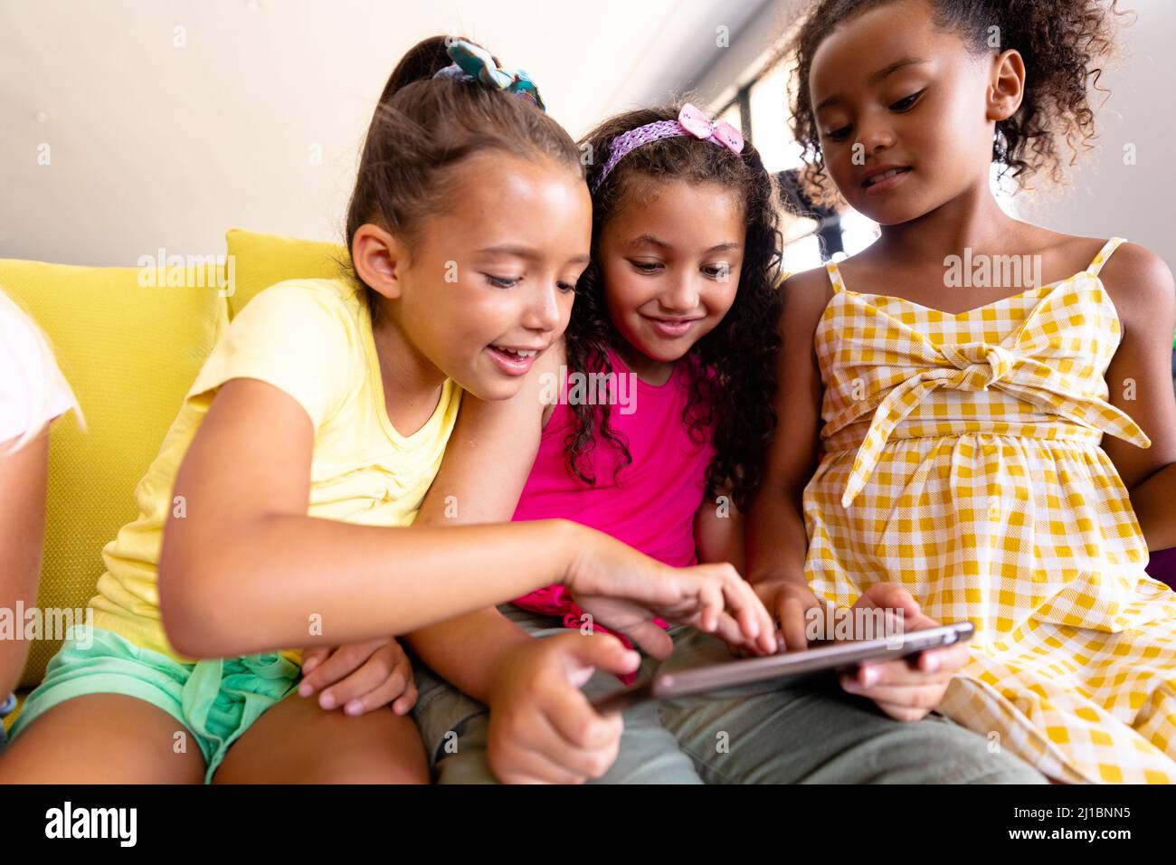 Lächelnde multirassische Grundschüler mit digitalem Tisch, während sie auf der Couch sitzen Stockfoto