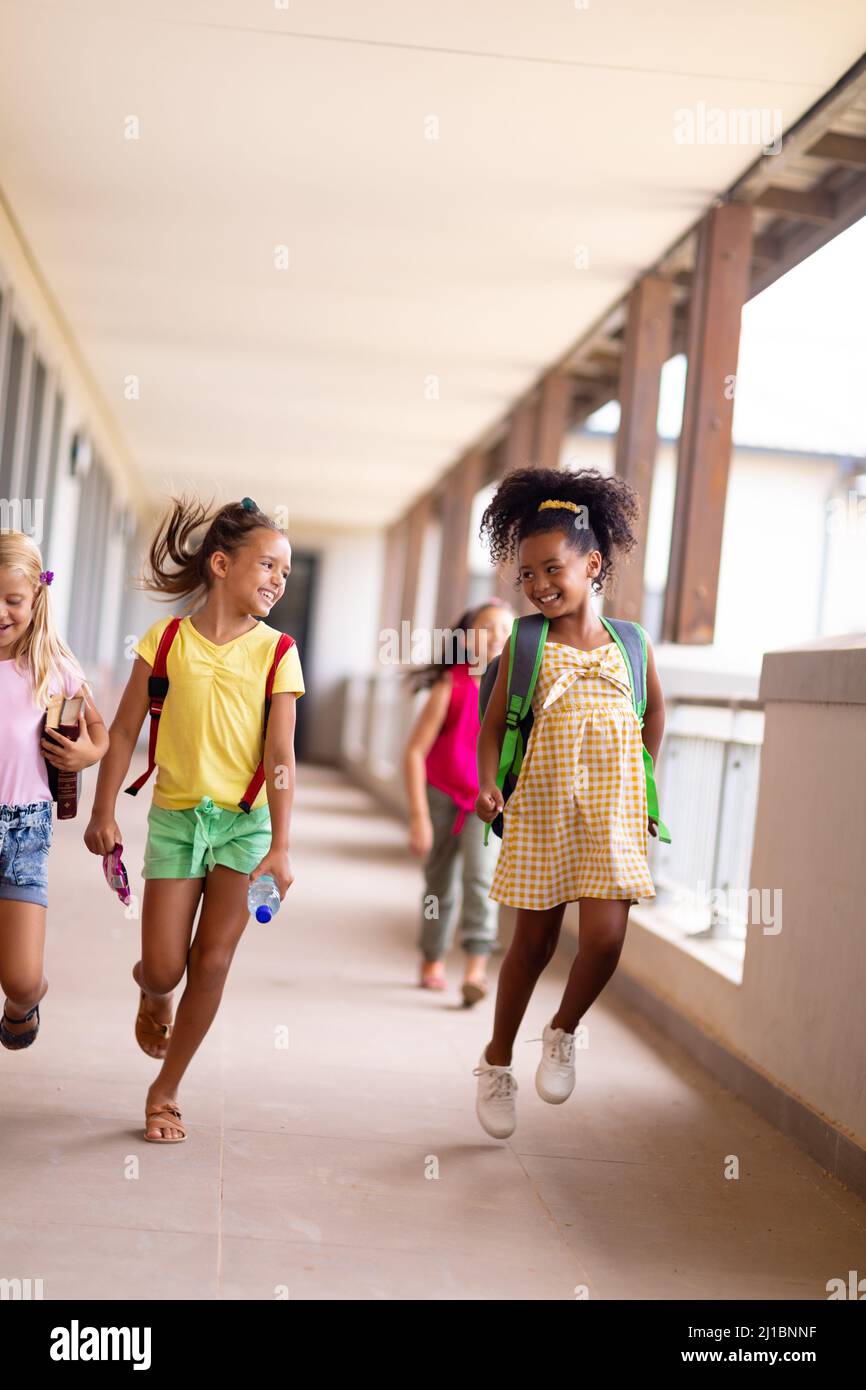 In voller Länge fröhliche multirassische Grundschüler gehen im Flur Stockfoto