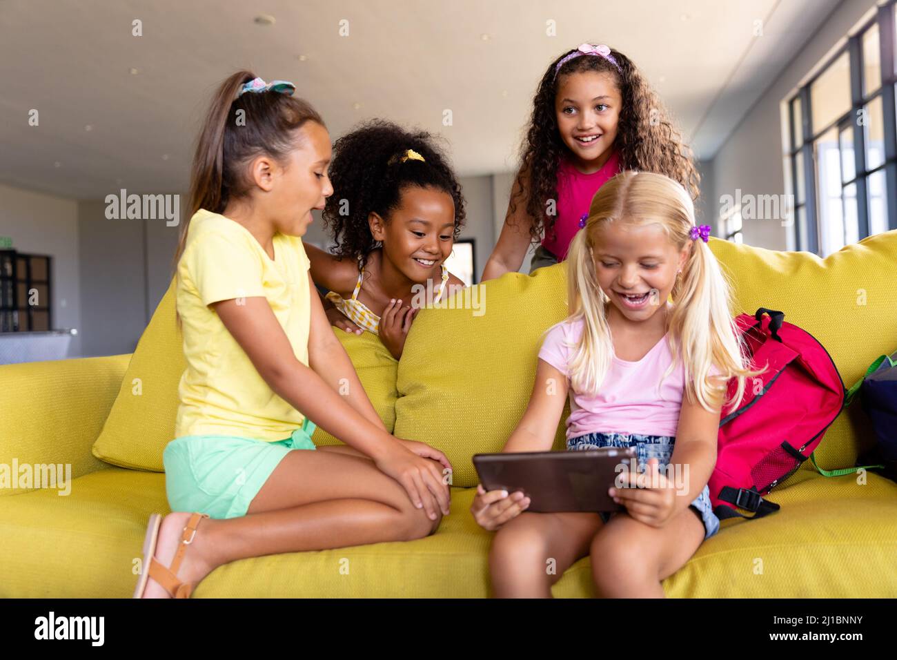 Fröhliche multirassische Grundschüler mit digitalen Tisch, während sie auf der Couch sitzen Stockfoto