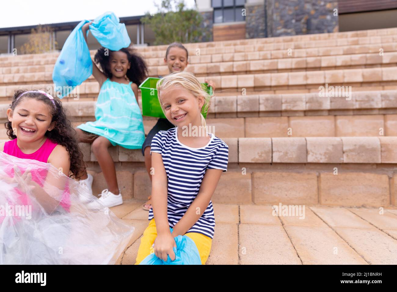 Fröhliche multirassische Grundschüler mit Mülltüten auf der Schultreppe Stockfoto