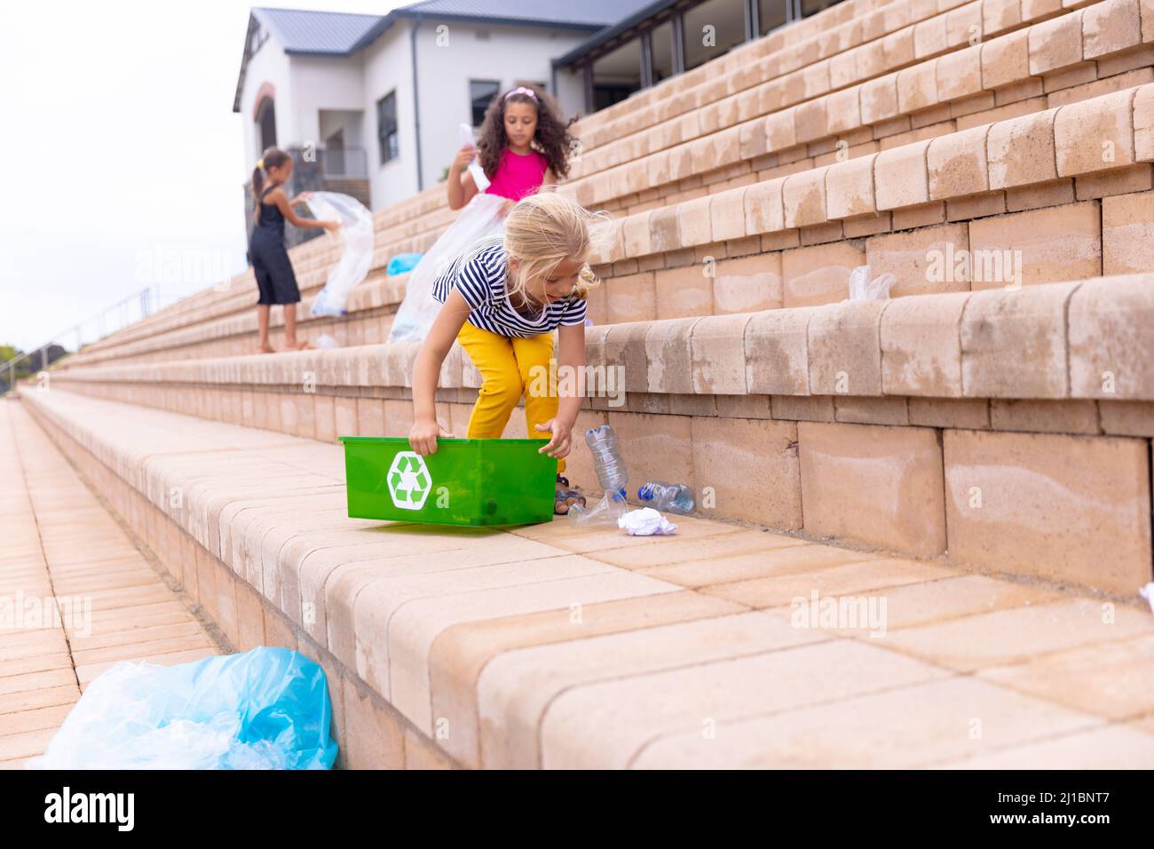 Multirassische Grundschüler, die Plastikmüll auf Schulbaustufen reinigen Stockfoto